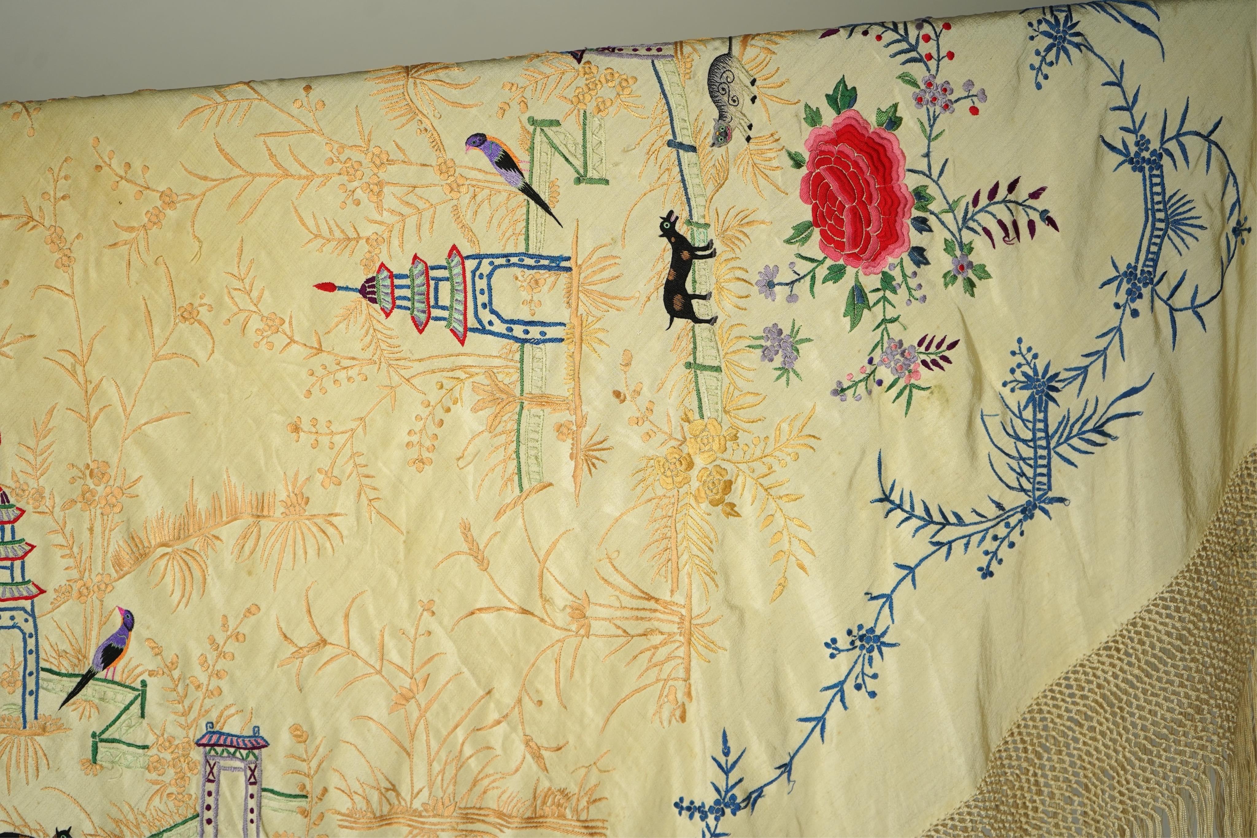 A Chinese cream silk polychrome embroidered shawl with a long fringe. Embroidered with four unusual corner cartouches of Pagoda, flowers, birds, cats and dogs. 132cm x 126cm.